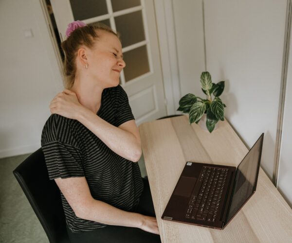 Kvinde med hold i nakken der sidder ved en computer